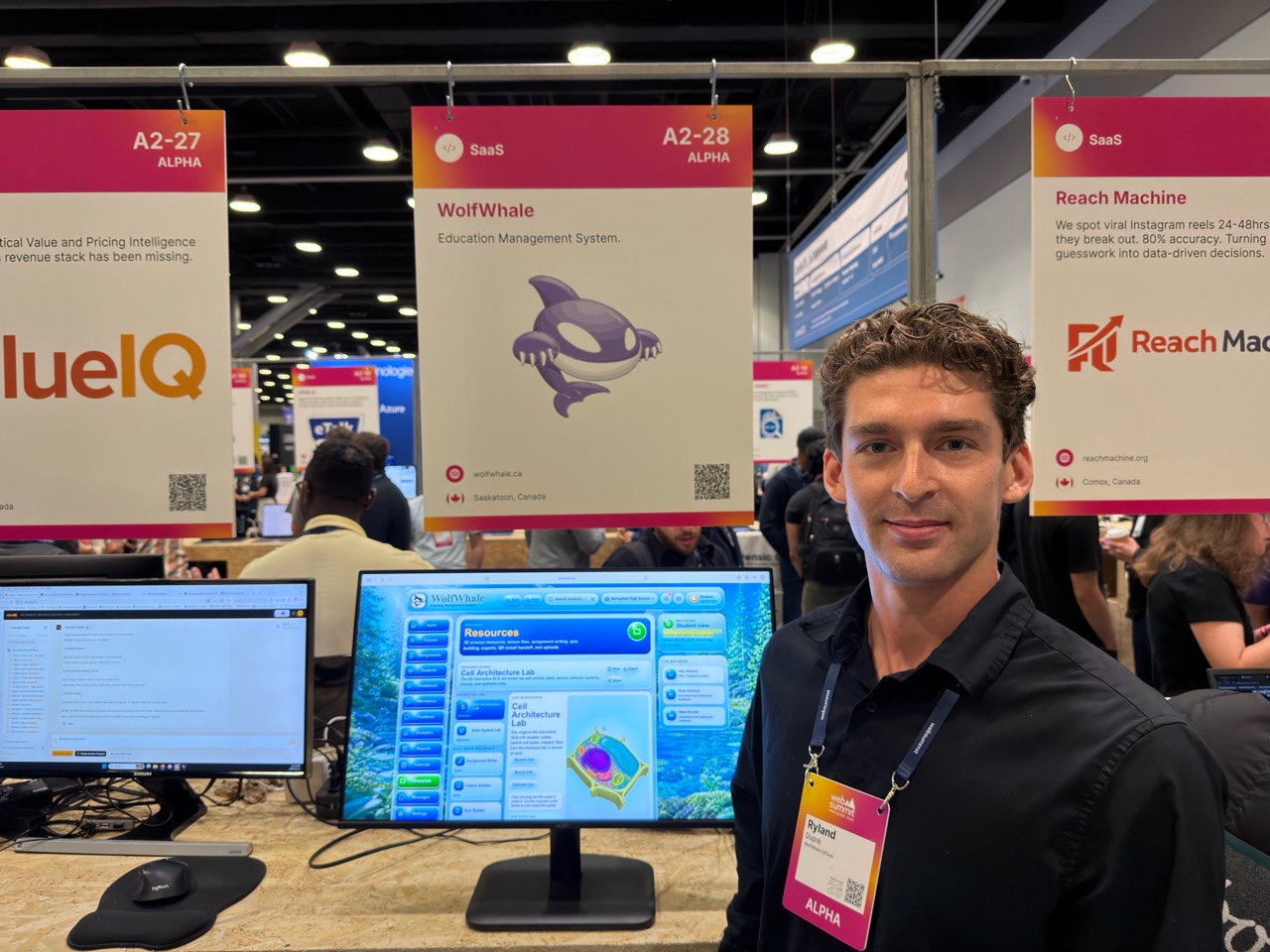 Ryland Dupré at the WOLFWHALE booth, with the education platform on a computer screen and the WOLFWHALE board behind him.